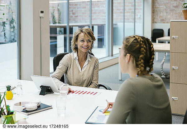 Smiling businesswoman discussing with female coworker at desk