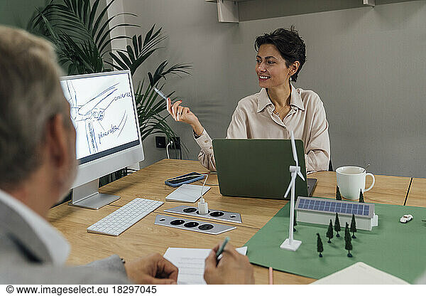 Smiling businesswoman explaining over computer at table in office