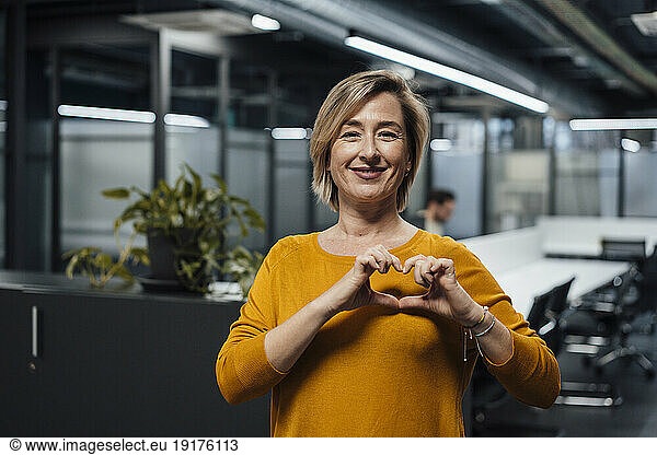 Smiling businesswoman gesturing heart shape at work place