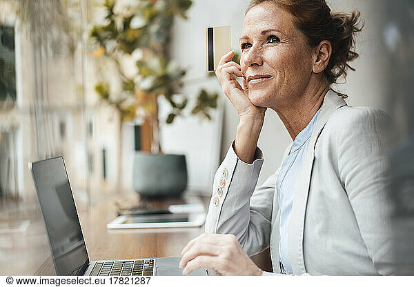 Smiling businesswoman holding credit card sitting with laptop in cafe