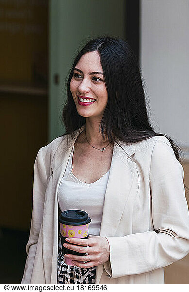 Smiling businesswoman holding disposable coffee cup in office