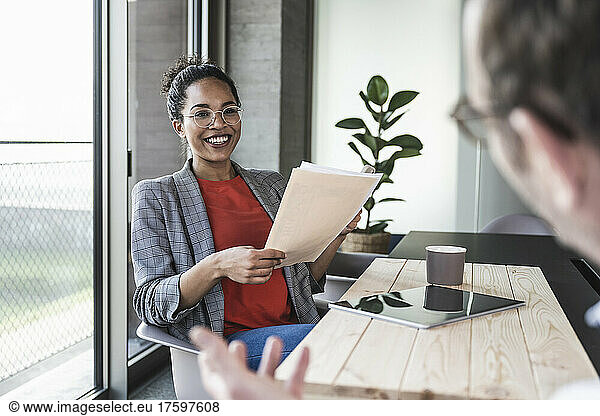 Smiling businesswoman holding documents discussing with colleague in office