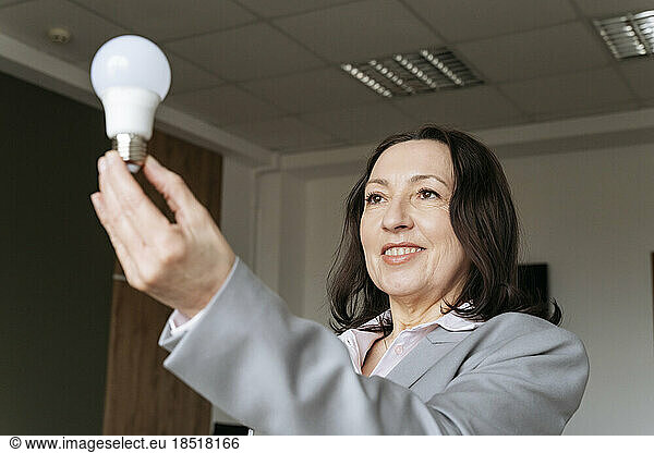 Smiling businesswoman holding electric bulb at office