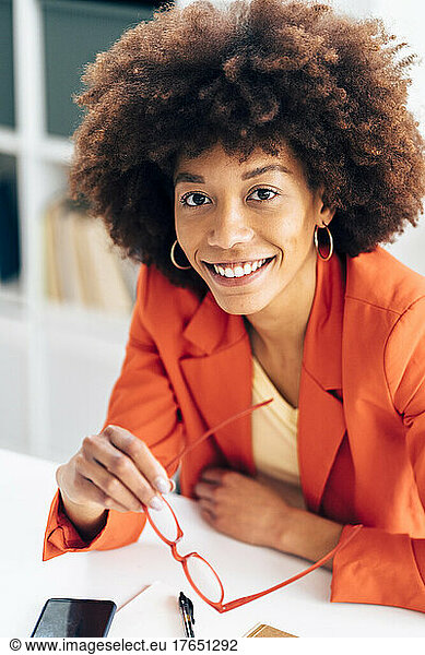 Smiling businesswoman holding eyeglasses sitting at desk