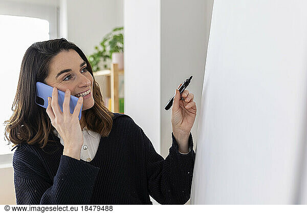 Smiling businesswoman holding felt tip pen and talking on smart phone
