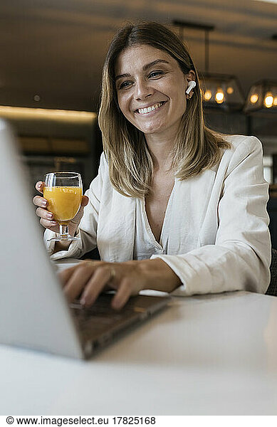 Smiling businesswoman holding juice glass using laptop at restaurant
