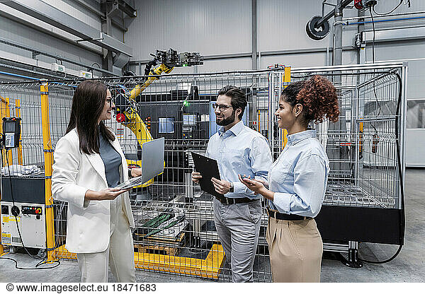 Smiling businesswoman holding laptop and having discussion with colleagues in factory
