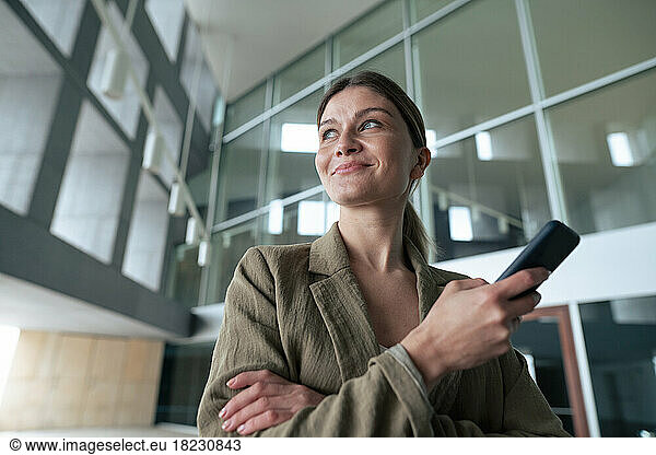 Smiling businesswoman holding mobile phone in lobby