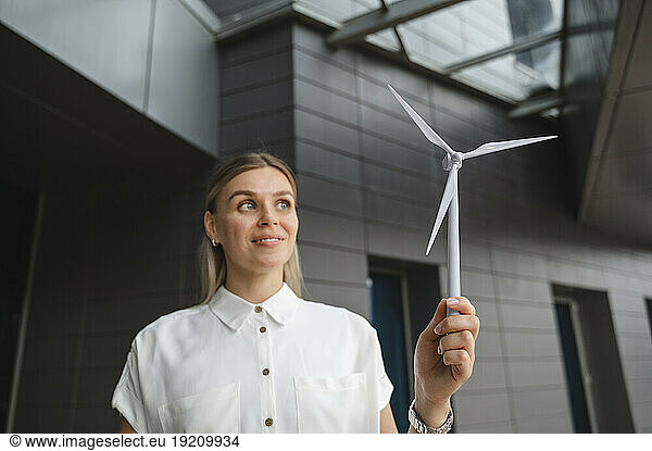 Smiling businesswoman holding model wind turbine