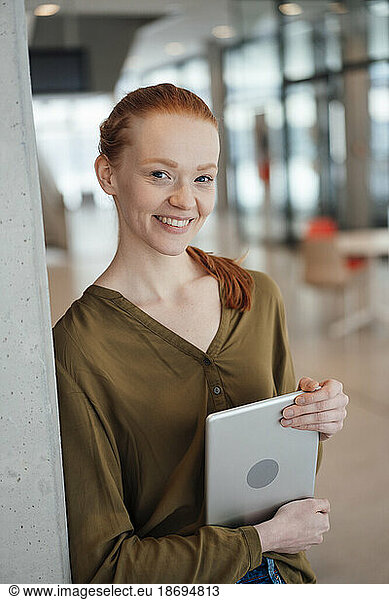 Smiling businesswoman holding tablet PC at office