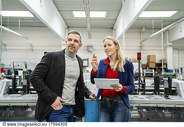 Smiling businesswoman holding tablet PC sharing ideas with colleague standing by machinery