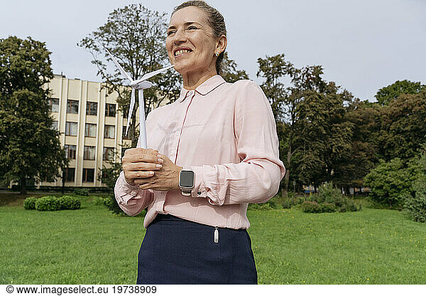 Smiling businesswoman holding wind turbine model in park