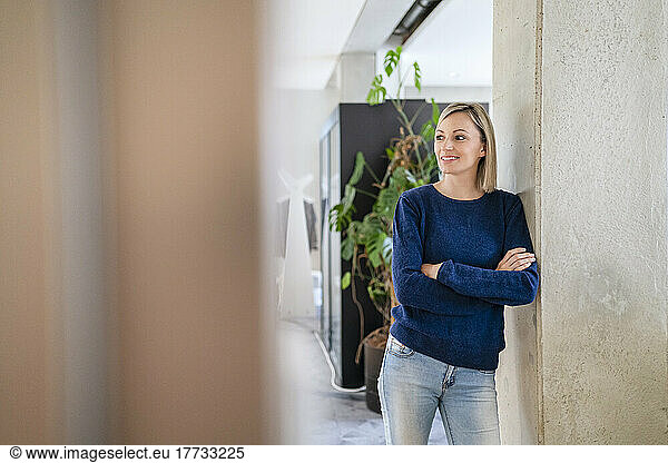 Smiling businesswoman leaning against column in office