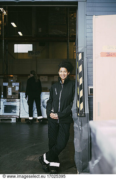 Smiling businesswoman leaning on wall at distribution warehouse