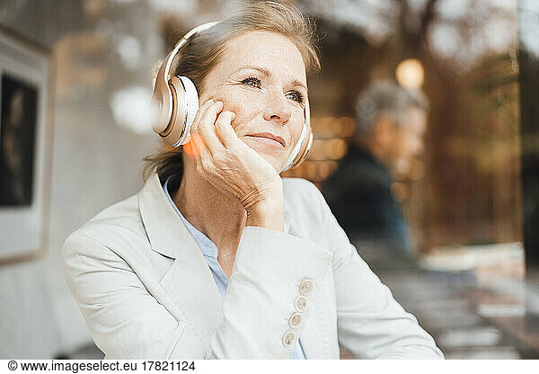 Smiling businesswoman listening music through wireless headphones in cafe