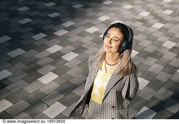 Smiling businesswoman listening to music through wireless headphones at sunny day