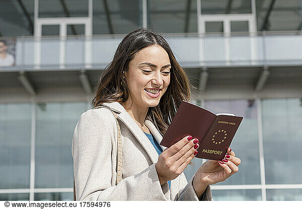 Smiling businesswoman looking at passport on sunny day