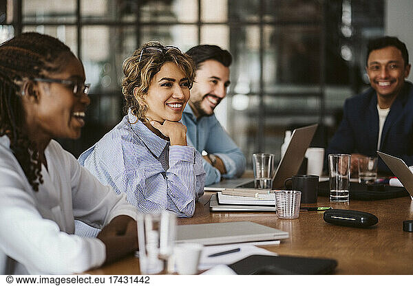 Smiling businesswoman looking away while sitting amidst colleagues at conference table