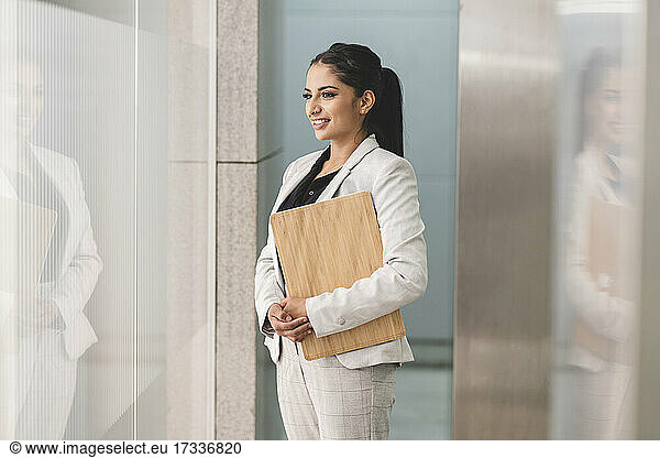 Smiling businesswoman looking through window while standing at office