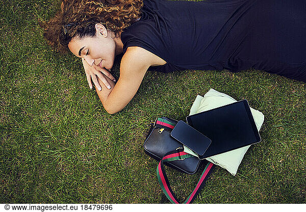 Smiling businesswoman lying by office stuff on grass at park