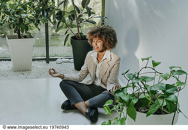 Smiling businesswoman practicing meditation near plants in office