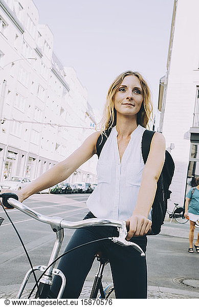 Smiling businesswoman riding bicycle on road in city against sky