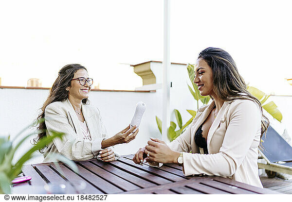 Smiling businesswoman showing dermopigmentation pen to colleague at table