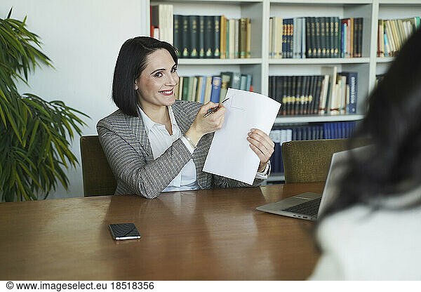 Smiling businesswoman showing document to colleague at office