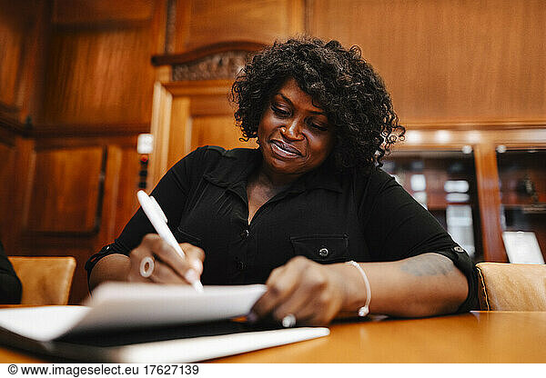 Smiling businesswoman signing contract document sitting at conference table in board room during meeting