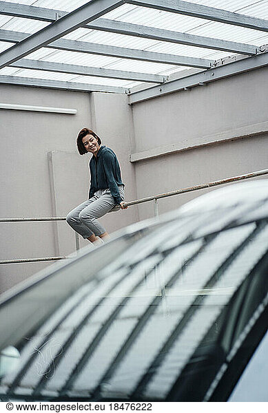 Smiling businesswoman sitting on railing in parking lot