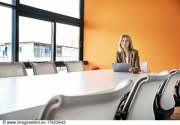 Smiling businesswoman sitting with digital tablet inboard room at office