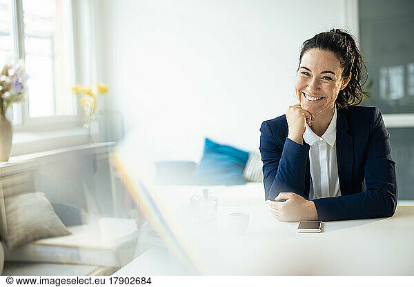 Smiling businesswoman sitting with hand on chin