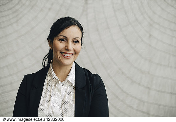 Smiling businesswoman standing against wall at office