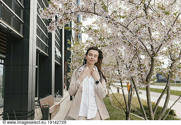 Smiling businesswoman standing in front of cherry blossom flower tree