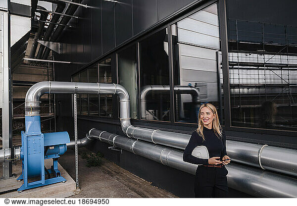 Smiling businesswoman standing near machine pipes in factory