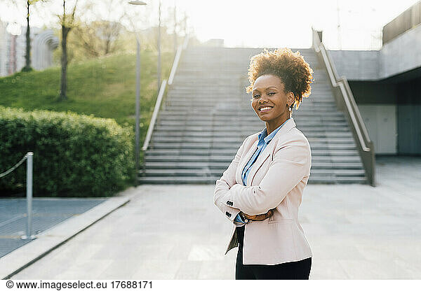 Smiling businesswoman standing with arms crossed in front of staircase