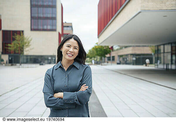 Smiling businesswoman standing with arms crossed near buildings