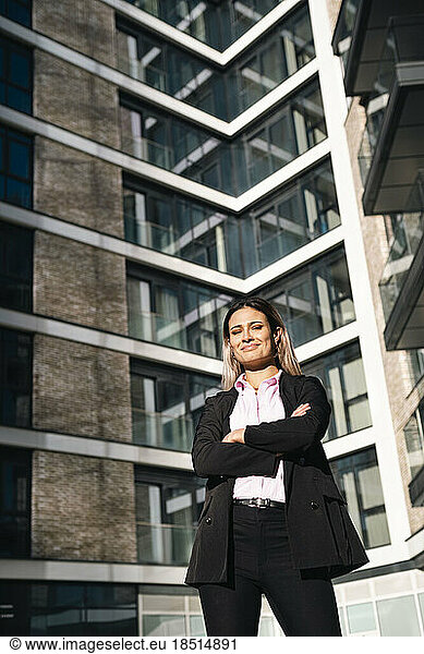 Smiling businesswoman standing with arms crossed outside office building
