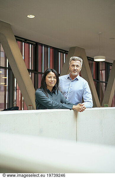Smiling businesswoman standing with businessman near wall
