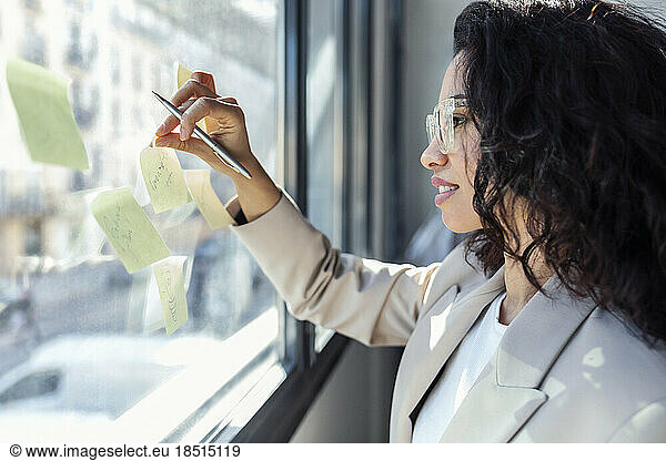 Smiling businesswoman sticking adhesive notes on glass window in studio