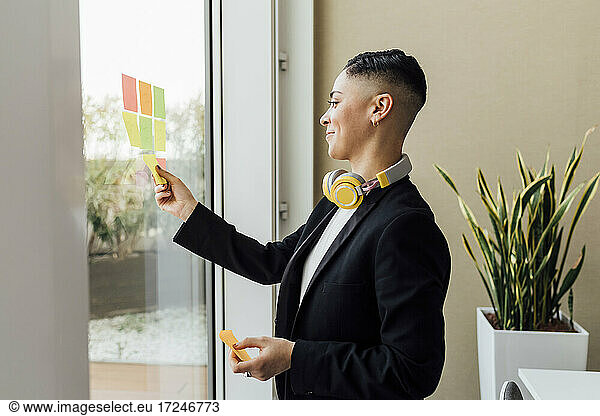 Smiling businesswoman sticking adhesive notes on window at office