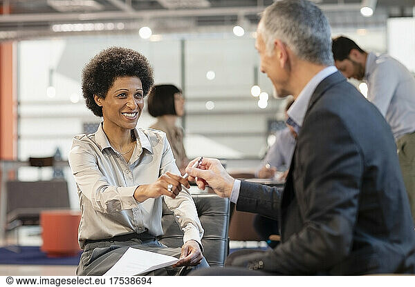 Smiling businesswoman taking pen from colleague in office