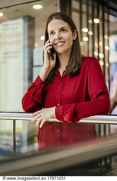 Smiling businesswoman talking on smart phone in office corridor