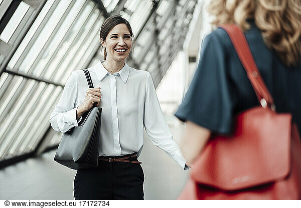 Smiling businesswoman talking with female colleagues in office corridor