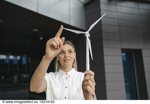 Smiling businesswoman touching wind turbine model