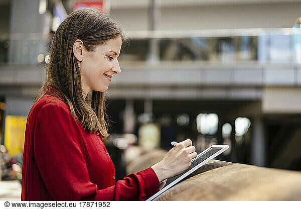 Smiling businesswoman using digitized pen on tablet PC at workplace