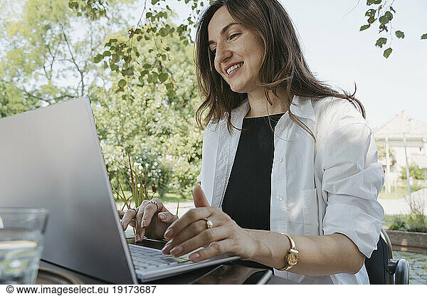 Smiling businesswoman using laptop at table in garden