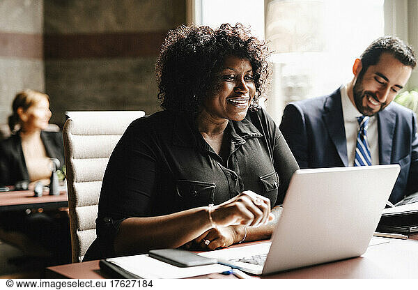 Smiling businesswoman using laptop by businessman sitting at desk working in law office