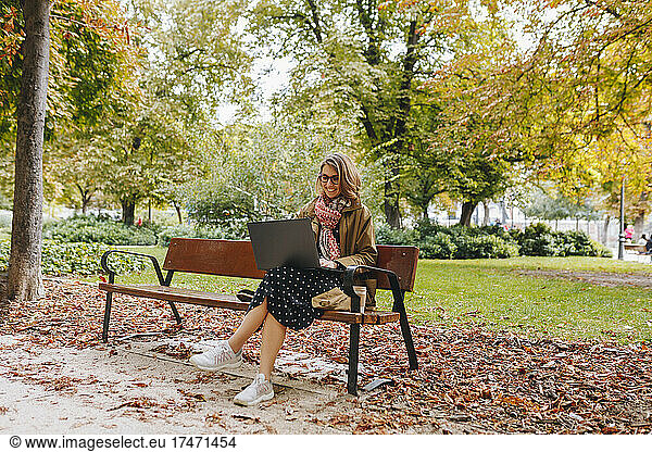 Smiling businesswoman using laptop on bench