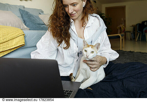 Smiling businesswoman using laptop with cat at home office